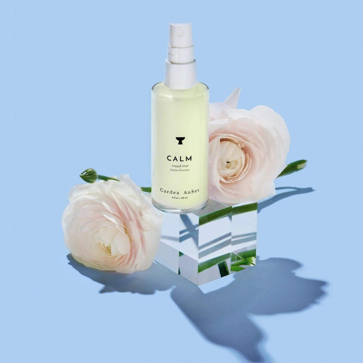 Calm Mood Mist bottle with white roses on a mirrored cube, ideal for relaxation and aromatherapy using lavender, bergamot, and frankincense.