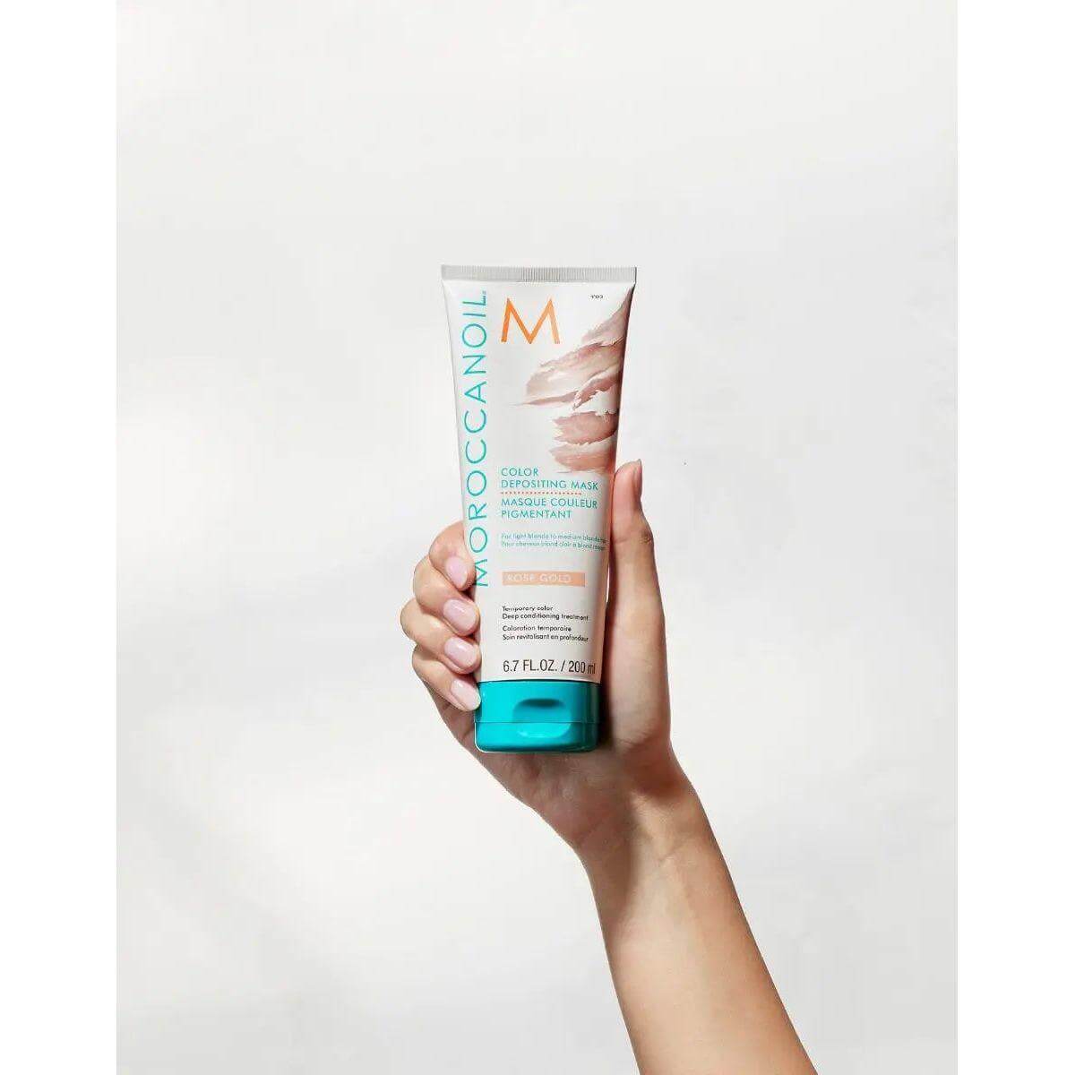 Hand holding Moroccanoil Color Depositing Mask tube for enhancing and conditioning hair color between salon visits.