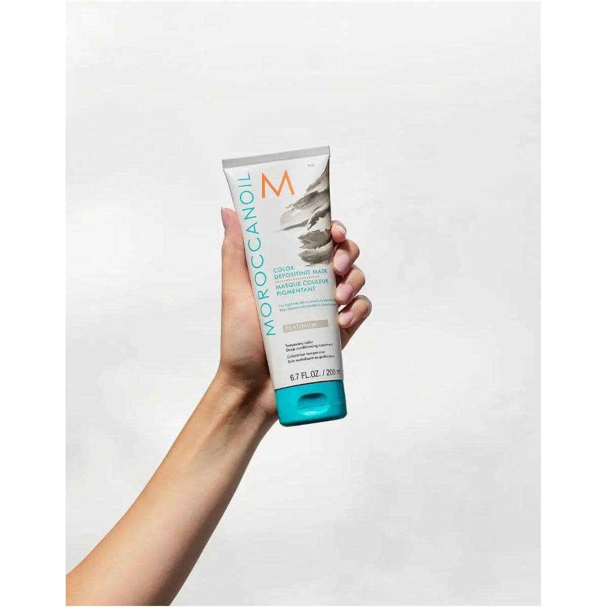 Hand holding Moroccanoil Color Depositing Mask, ideal for enhancing tone, refreshing hair color, deep conditioning, and adding shine.