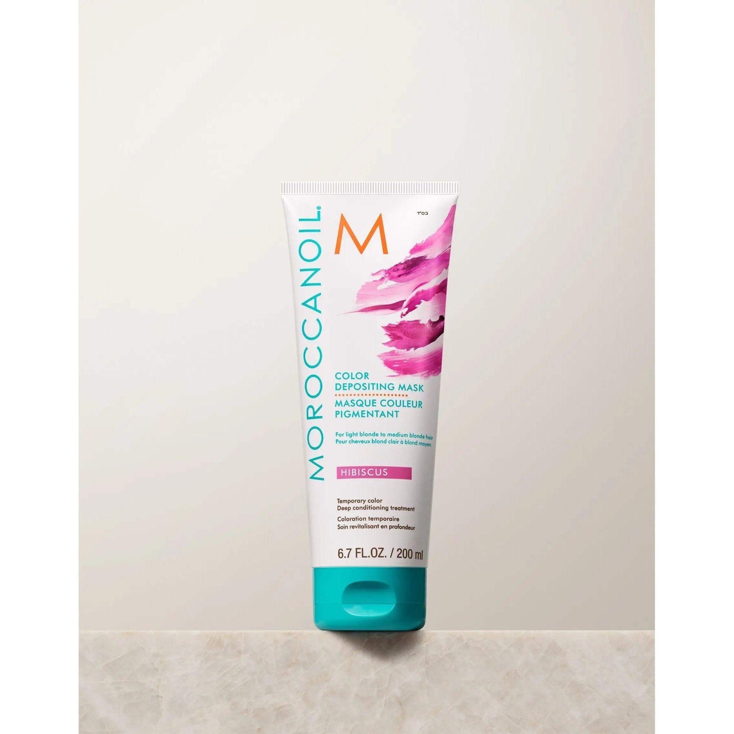 Moroccanoil Color Depositing Mask tube on a marble surface, for toning and refreshing hair color with deep conditioning benefits.