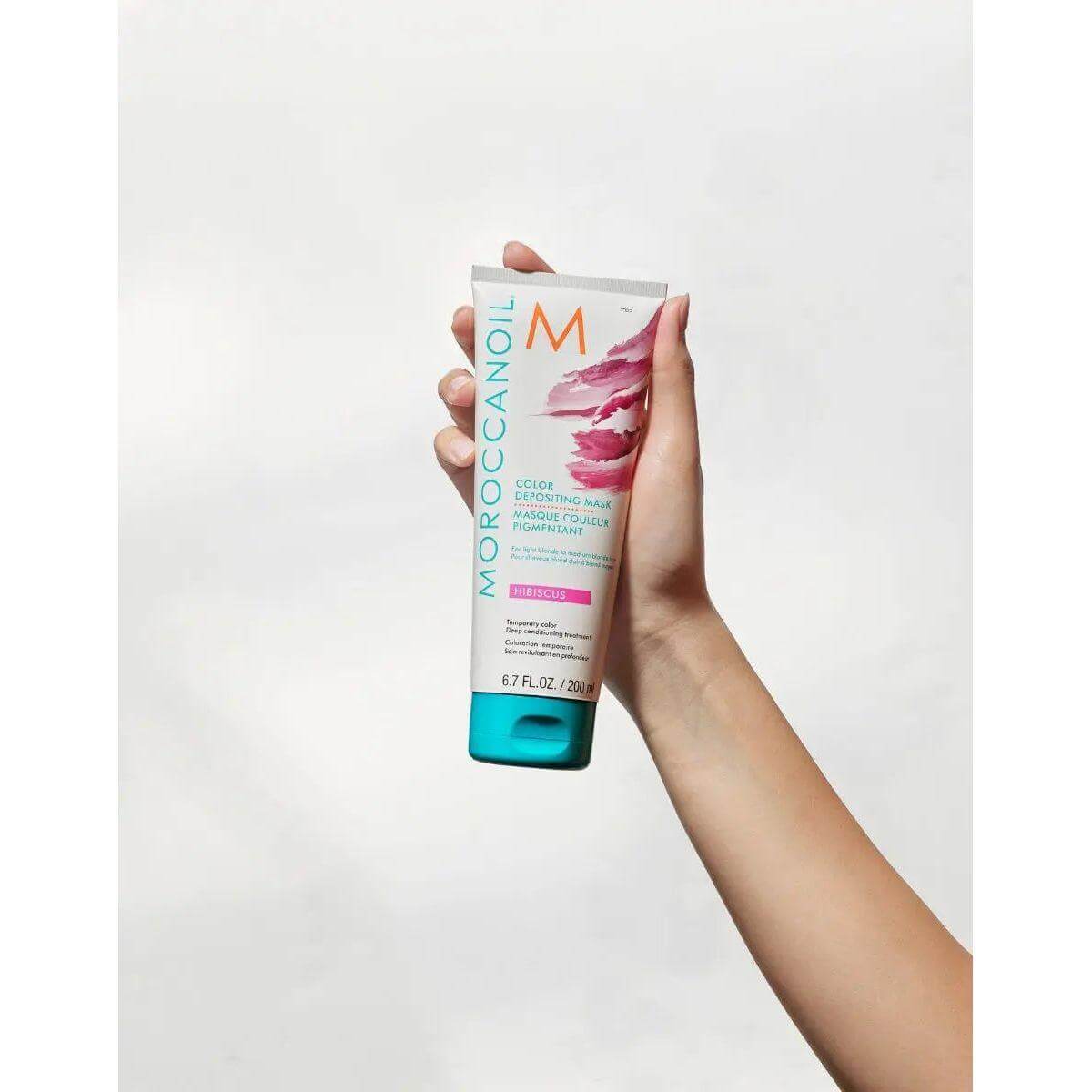Hand holding Moroccanoil Color Depositing Mask for rejuvenating and softening hair, enhancing and refreshing tone between salon visits.