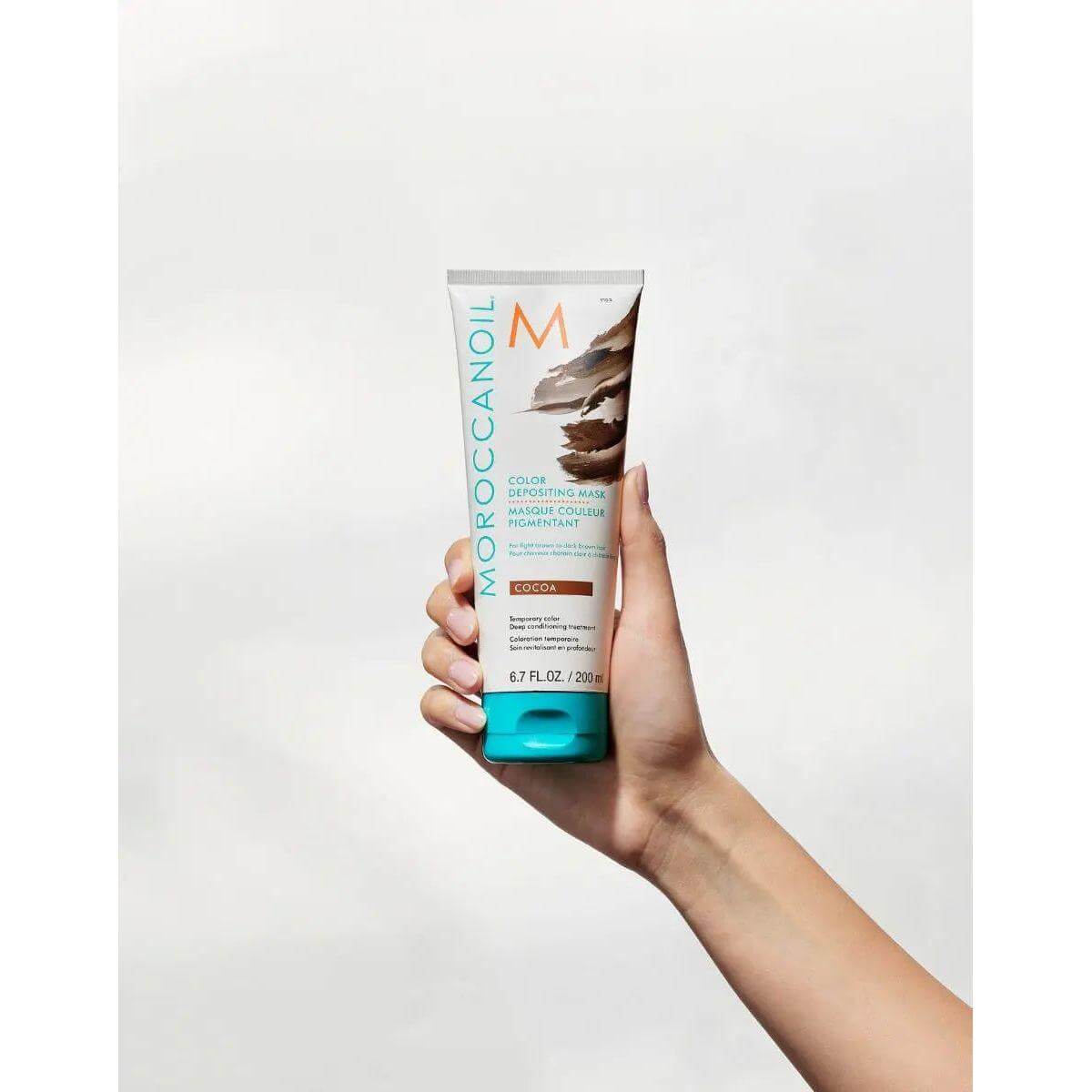 Hand holding Moroccanoil Color Depositing Mask, rejuvenates and enhances hair tone, increases softness and imparts radiant shine.