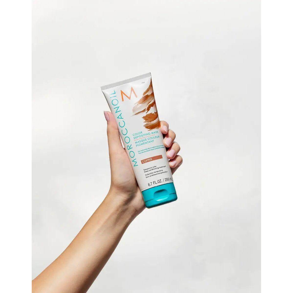 Hand holding Moroccanoil Color Depositing Mask, ideal for hair color enhancement and deep conditioning.