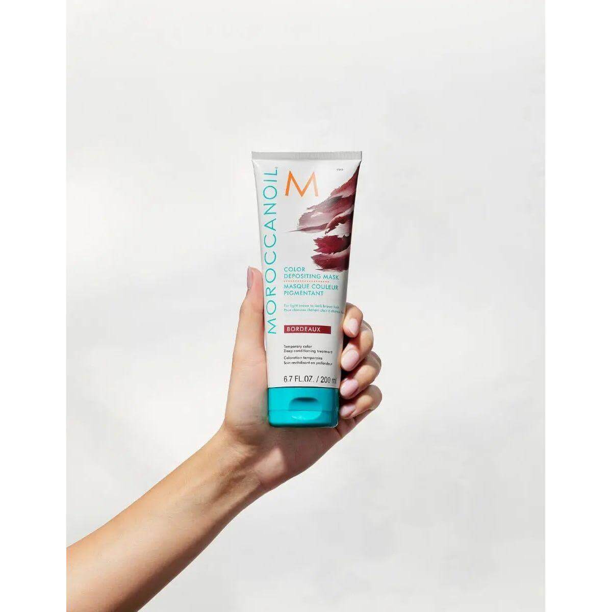 Hand holding Moroccanoil Color Depositing Mask, ideal hair treatment for softness, shine, and refreshed color.
