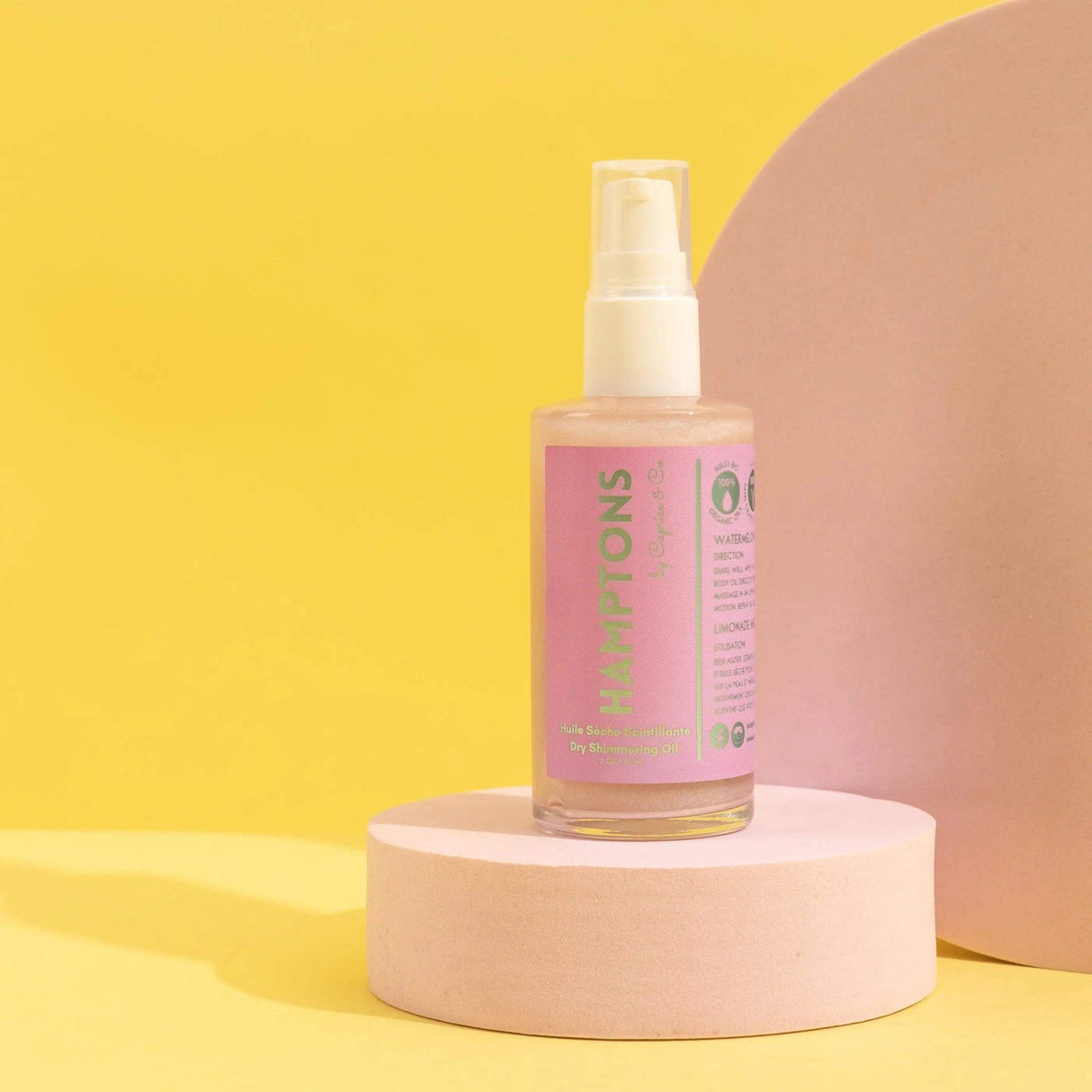 Hamptons Dry Shimmering Oil with pink tint on round pedestal, 2 oz bottle. Organic ingredients, illuminating watermelon lemonade scent.