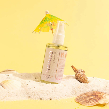 Monaco Dry Miracle Oil bottle on sand with seashells, featuring white freesia and vanilla scent, 2 oz size organic dry body oil.
