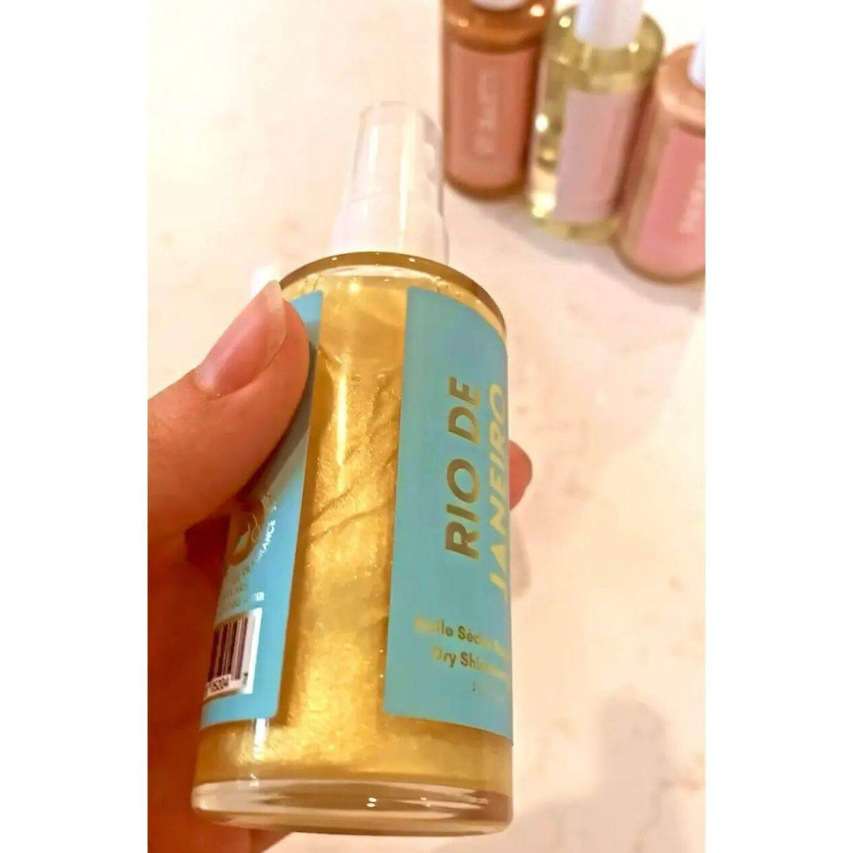 Hand holding a bottle of Rio De Janeiro Dry Shimmering Oil with yellow gold tint, lime and coconut scent, 2 oz size.