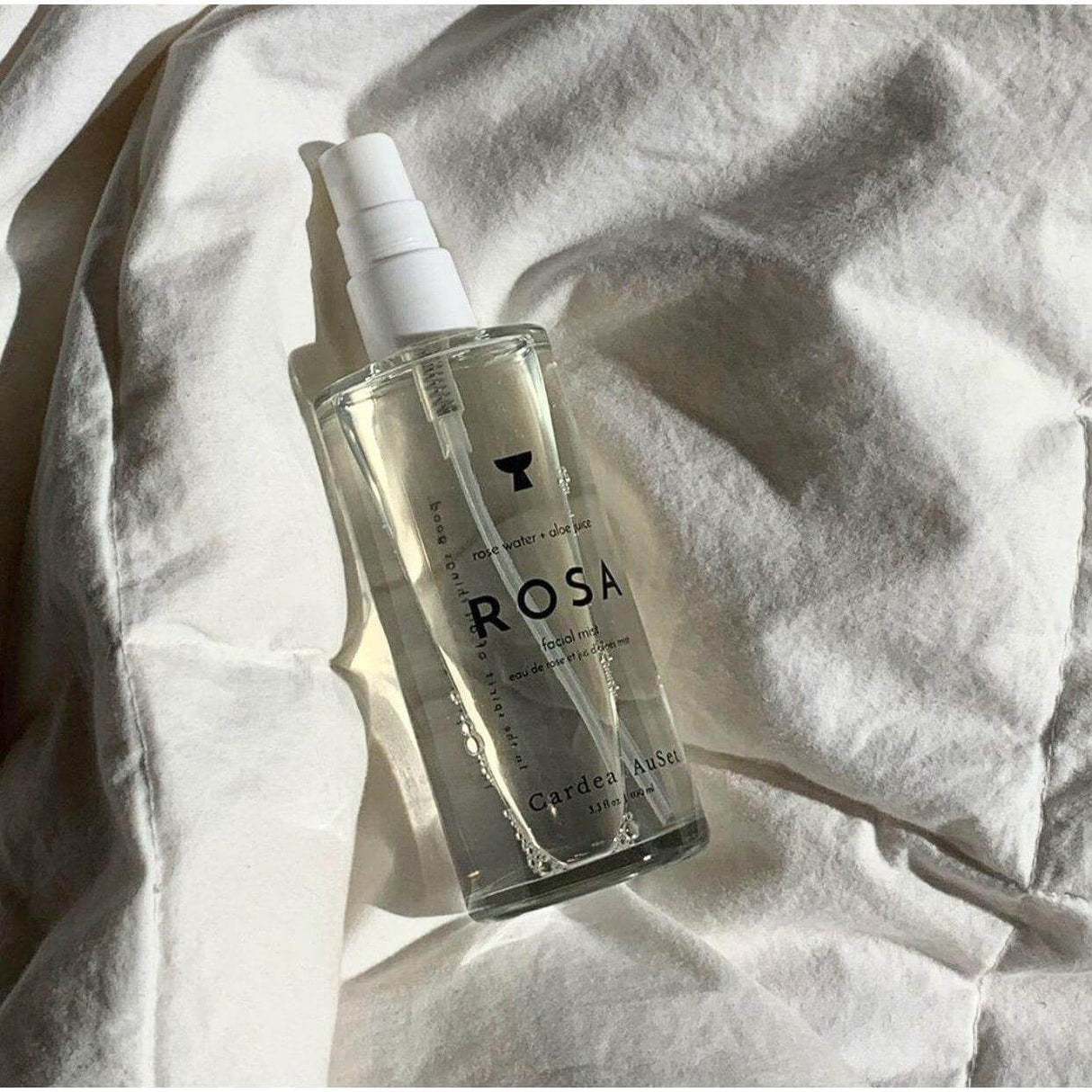 Rosa Facial Mist bottle on fabric, ultra-hydrating rose water and aloe mist for refreshed, plump skin, reduces redness and inflammation.