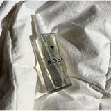 Rosa Facial Mist bottle on fabric, ultra-hydrating rose water and aloe mist for refreshed, plump skin, reduces redness and inflammation.